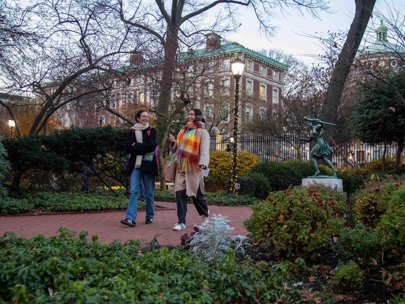 学生 walk on Barnard campus with holiday lights and runner statue in background